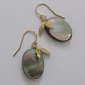 May include: A pair of gold earrings featuring oval, iridescent, grey-green stones. Each earring has a small gold leaf design and a hook for pierced ears. The earrings are presented on a white surface.