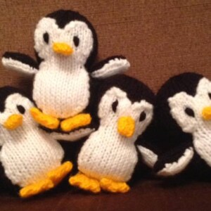 Può includere: Un gruppo di cinque pinguini di lana. Ogni pinguino ha un corpo bianco, testa e ali nere, e piedi e becco gialli. I pinguini sono disposti in una composizione giocosa, leggermente sovrapposta.