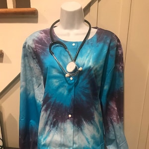 May include: A blue and purple tie-dye scrub top with a button-up front and long sleeves. A black stethoscope is draped around the neck of the scrub top.