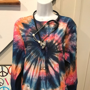 May include: A tie-dye medical scrub top with long sleeves and a button-up front. The scrub top has a stethoscope around the neck.