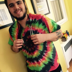 May include: A person wearing a tie-dye shirt with a stethoscope around their neck. The shirt is a mix of red, green, yellow, and black.