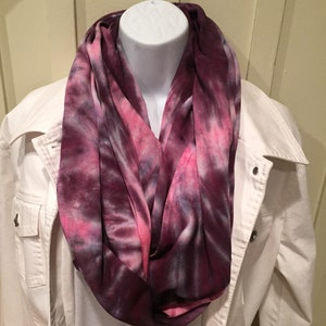 May include: A purple, pink, and white tie-dye infinity scarf. The scarf is made of a soft, comfortable fabric and is perfect for adding a pop of color to any outfit.