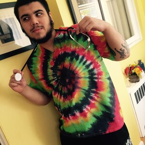 May include: A person wearing a tie-dye shirt with a stethoscope around their neck. The shirt has a red, green, yellow, and black swirl pattern.