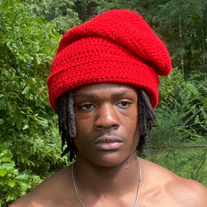 May include: A red crocheted beanie with a slouchy fit. The beanie is worn by a person with dreadlocks. The person has a tattoo on their chest that reads "Proverbs 22:34", "Get a little sleep, a little slumber, a little folding of the hands to rest".