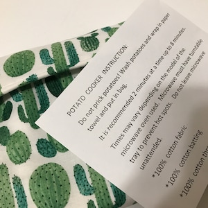 May include: A white and green cactus-patterned potato cooker with a printed instruction sheet. The instructions advise washing potatoes, wrapping them in paper, and microwaving them for up to 8 minutes.