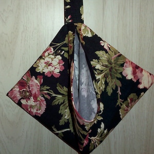 Könnte beinhalten: Eine rautenförmige Stofftasche mit einem Blumenmuster in Rosa, Grün und Creme auf schwarzem Hintergrund. Die Tasche hat oben eine Schlaufe zum Aufhängen und eine kontrastierende rote Paspel.