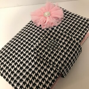May include: A black and white houndstooth pattern clutch with a pink flower embellishment. The flower has a pearl center and rhinestone accents. The clutch has a button closure and a pink interior.