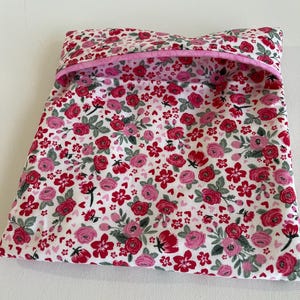 May include: A pink and red floral print fabric pouch with a pink trim. The pouch is folded closed and is lying on a white surface.