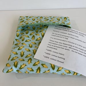 May include: A light blue fabric pouch with a corn pattern. The pouch is filled with potatoes and is used for cooking potatoes in the microwave. The pouch has instructions for using the potato cooker in the microwave. The instructions say to microwave in 2 minute intervals, no longer than 8 minutes total. Do not prick potatoes, wash potatoes and towel and put in bag. It is recommended 2 minutes at a time up to 8 minutes. Times may vary depending on the model of microwave oven used. Microwave must have a tray to prevent hot spots. Do not leave microwave unattended. The pouch is made of 100% cotton fabric, 100% cotton batting, and 100% cotton thread.