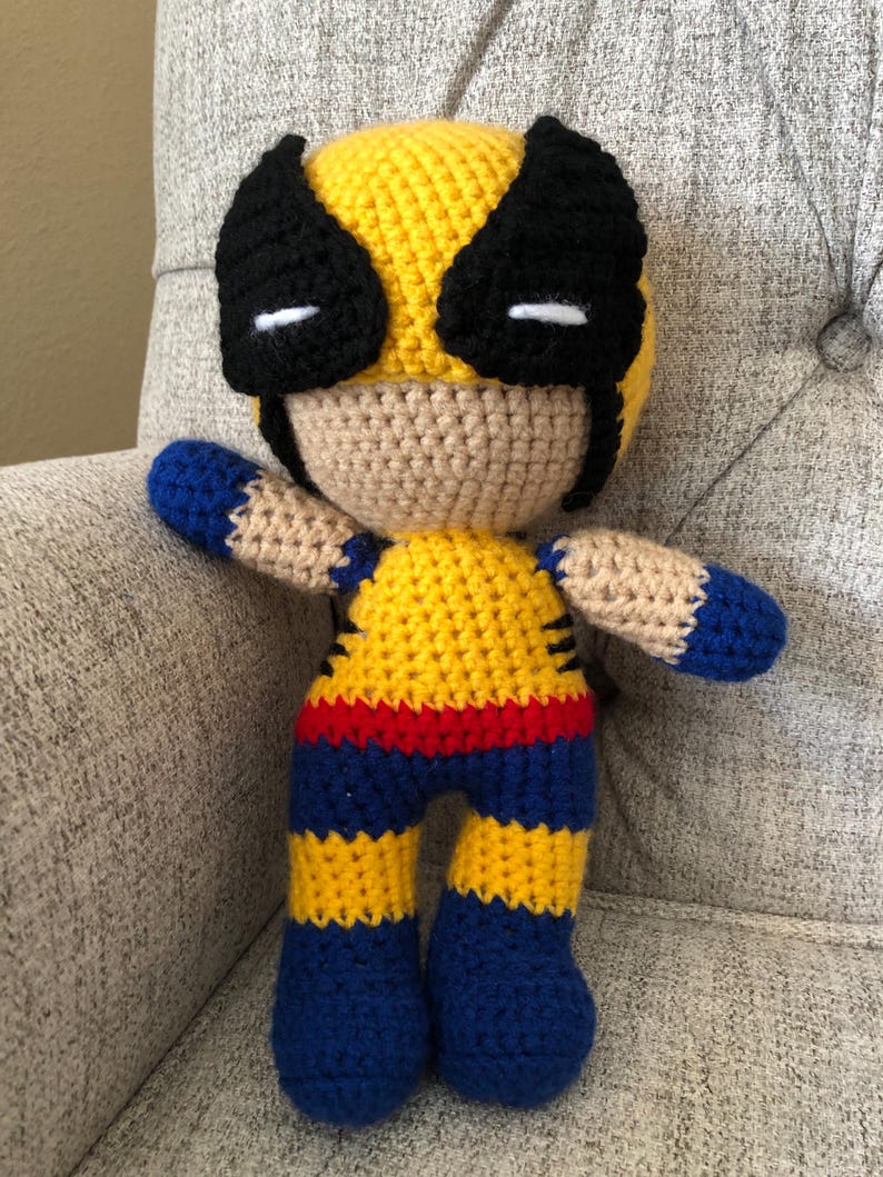 Op de afbeelding: Een handgemaakte gehaakte pop die Wolverine voorstelt. De pop heeft een geel en zwart masker, een geel en blauw kostuum en een bruine huid. De pop is ongeveer 25 cm hoog en is gemaakt van garen. Een uniek, handgemaakt item.