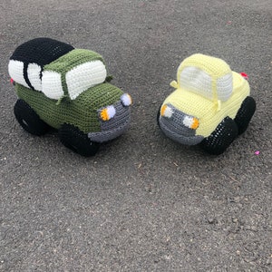 May include: Two crocheted toy cars, one green with a black roof and one yellow. Both cars have black wheels and gray details.