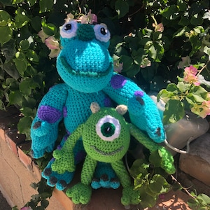 May include: Two crocheted plush toys, one blue with purple spots and one green with one large eye, inspired by the characters from the movie Monsters Inc.