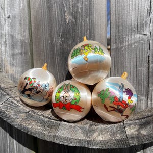 Könnte beinhalten: Vier vintage Weihnachtskugeln mit Satin-Finish. Jede Kugel zeigt einen anderen Cartoon-Charakter aus der Looney Tunes-Serie: Bugs Bunny, Tweety Bird, Sylvester die Katze und Road Runner.