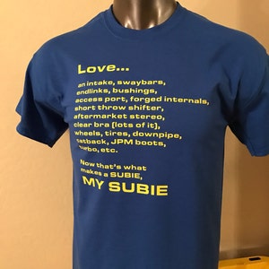 以下が含まれることがあります： 「Love... an intake, swaybars, endlinks, bushings, access port, forged internals, short throw shifter, aftermarket stereo, clear bra (lots of it), wheels, tyres, downpipe, catback, JPM boots, turbo, etc. Now that's what makes a SUBIE, MY SUBIE」と黄色い文字で書かれた青いTシャツ。