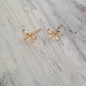 May include: A pair of gold bow-shaped stud earrings. The earrings are small and delicate, and they would make a great gift for a special occasion.