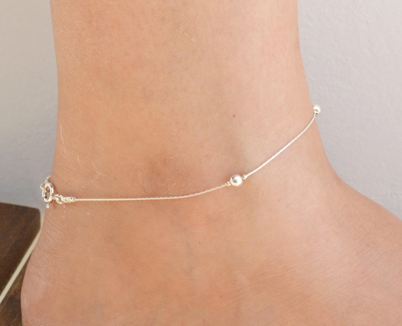 May include: A delicate silver anklet with small round beads. The anklet is made of a thin chain and has a simple, elegant design.