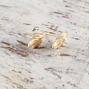May include: A pair of gold leaf-shaped earrings. The earrings are small and delicate, with a textured surface.