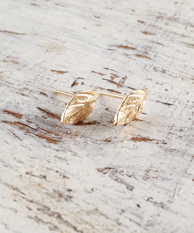 May include: A pair of gold leaf-shaped earrings. The earrings are small and delicate, with a textured surface.