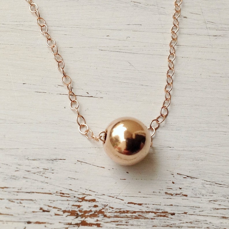 Puede incluir: Un delicado collar de cadena de oro con un solo colgante de cuentas redondas de oro.