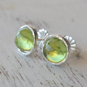 May include: A pair of silver earrings with green gemstone cabochons. The earrings have a hammered texture and a round shape.