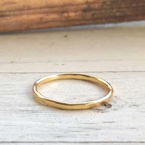 Pu&ograve; includere: Un delicato anello d'oro con una texture martellata. L'anello &egrave; sottile e ha un design semplice ed elegante. L'anello &egrave; posto su uno sfondo di legno chiaro. Questo anello &egrave; un gioiello.