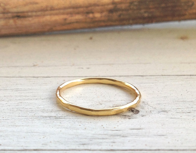 Pu&ograve; includere: Un delicato anello d'oro con una texture martellata. L'anello &egrave; sottile e ha un design semplice ed elegante. L'anello &egrave; posto su uno sfondo di legno chiaro. Questo anello &egrave; un gioiello.