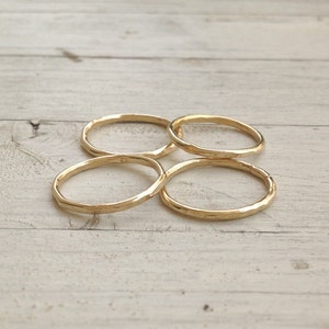Pu&ograve; includere: Quattro anelli dorati martellati sono disposti su una superficie di legno chiaro. Gli anelli hanno un aspetto strutturato e un design semplice e minimalista. Gli anelli sono circolari e sembrano essere di metallo.