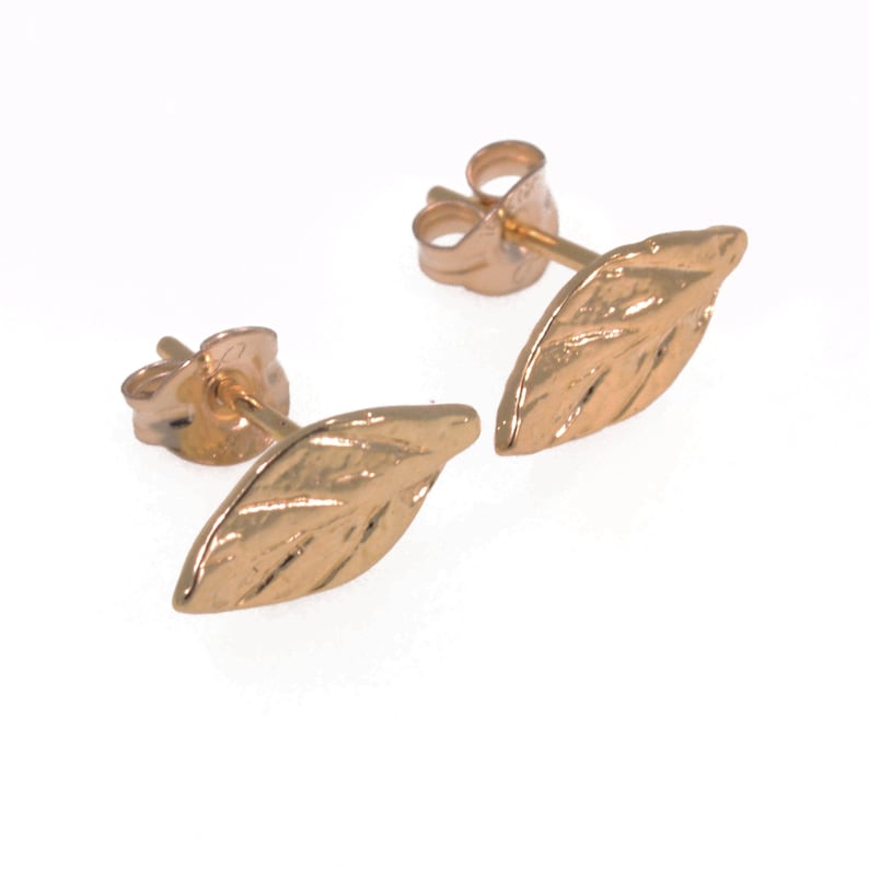 May include: A pair of gold leaf stud earrings. The earrings are made of a delicate, textured metal and have a simple, elegant design.