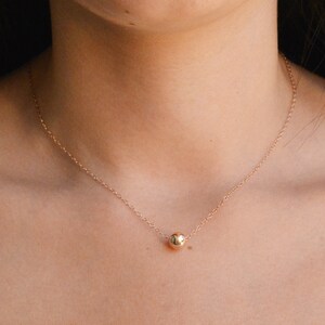 Puede incluir: Un delicado collar de cadena de oro con un solo colgante de cuentas redondas de oro.