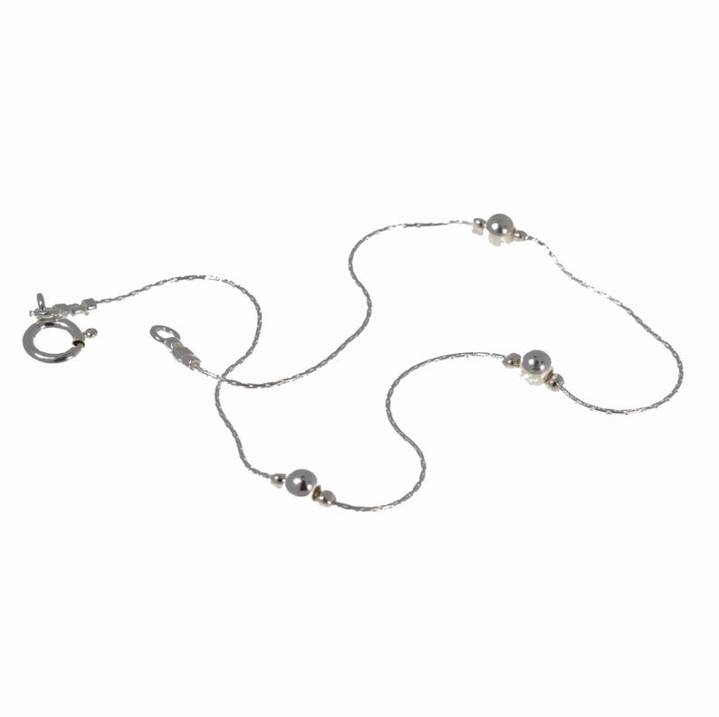 May include: A silver chain necklace with three silver beads.