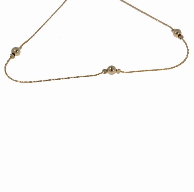 May include: A delicate gold chain necklace with small round beads. The chain is thin and has a braided design.