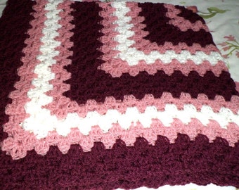 May include: A crocheted blanket with a burgundy, pink, and white geometric pattern.