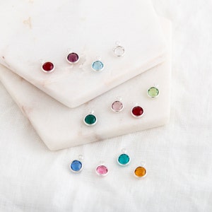 May include: Assortment of colorful crystal charms with silver settings. The charms are arranged on a white marble surface.