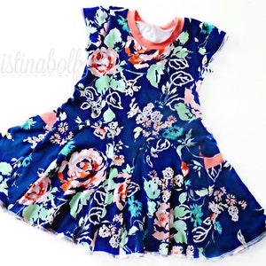 Könnte beinhalten: Marineblaues Kleid mit floralem Muster mit rosa, weißen und mintgrünen Blumen. Das Kleid hat einen korallenfarbenen Ausschnitt und Akzente an den Taschen. Das Kleid ist mit kurzen Ärmeln und einem ausgestellten Rock versehen.