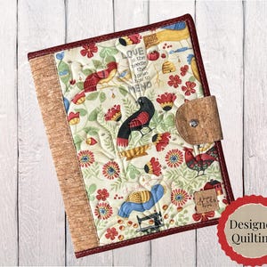 May include: A quilted fabric notebook cover featuring a cream background with colorful illustrations of birds, flowers, and sewing machines. The text reads LOVE is the needle that knows how to mend. It has a cork spine and a cork tab closure.
