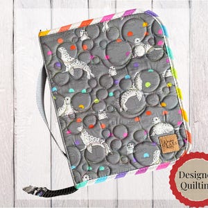 May include: A quilted gray zippered case featuring a repeating pattern of spotted seals and circular bubbles in neon orange, yellow, and teal. The fabric has a textured, wavy stitch pattern and a small tan rectangular label with the text "Whiskey Glass" attached to the lower right corner.