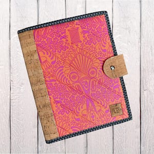May include: A quilted journal with a vibrant orange and pink floral pattern. The cover features a cork spine and a cork closure with a silver snap. The journal is trimmed with a black and gray patterned border.