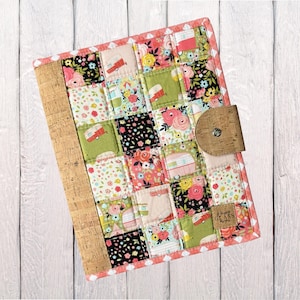 May include: A rectangular fabric notebook cover featuring a patchwork design of floral and camper trailer patterns in pink, green, black, and white. It includes a cork spine and a cork tab closure with a metal snap, plus a small cork brand label.
