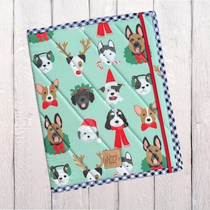 May include: A quilted, mint green fabric item featuring a repeating pattern of various dog breeds in festive attire. The item has a black and white checkered border, a red stripe, and a label that reads "Happy Glass".