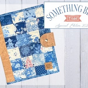 May include: A fabric book cover featuring a patchwork design of blue and white floral, botanical, and pagoda patterns. It includes a natural cork spine and a matching cork closure tab with a metal snap. A small square cork label is attached.