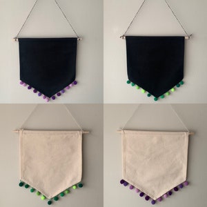 May include: Two black and two beige fabric banners with a pointed bottom edge. Each banner has a row of pom-poms along the bottom edge. The pom-poms are purple and green.