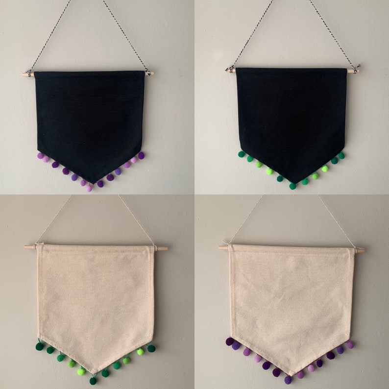 May include: Two black and two beige fabric banners with a pointed bottom edge. Each banner has a row of pom-poms along the bottom edge. The pom-poms are purple and green.