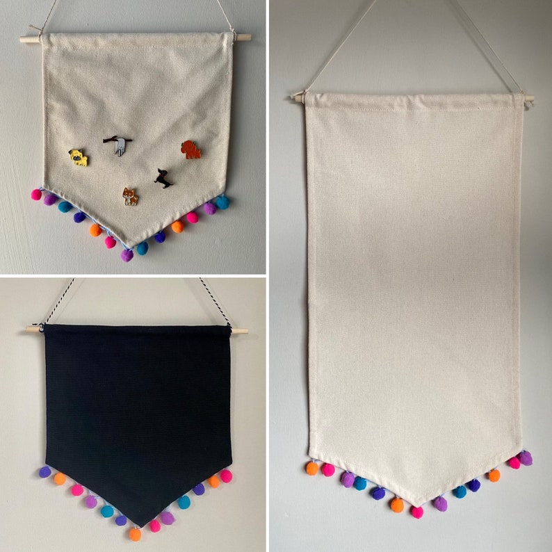 May include: Three fabric banners with pom pom trim. The first banner is white with a variety of colorful pins attached. The second banner is white and the third banner is black.