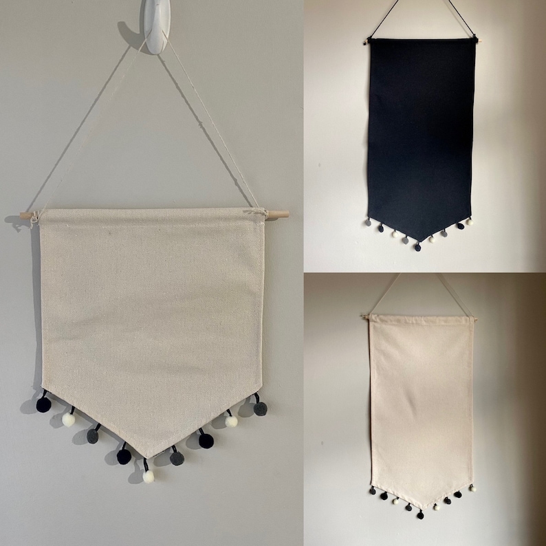 May include: Three fabric banners with pom pom trim. The banners are hanging from a wall. The banners are white, black, and beige.