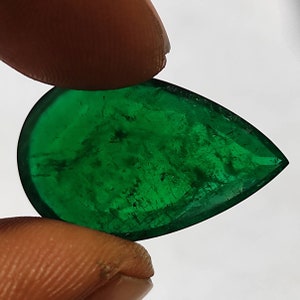 May include: A pear-shaped emerald gemstone with a deep green color. The gemstone has a faceted cut and is set in a clear, transparent setting.