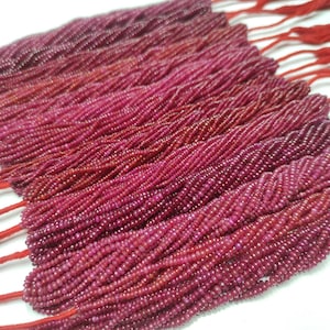 Może przedstawiać: Szereg koralików w kolorze rubinowej czerwieni, każdy koralik jest mały i okrągły. Koraliki są nawleczone na czerwoną nić i ułożone w rzędach.