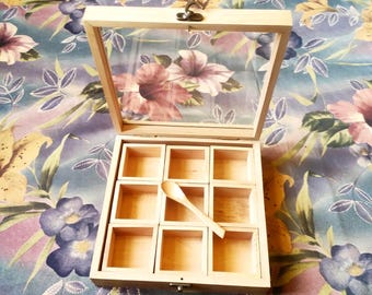Op de afbeelding: Een houten kruidenbox met een helder glazen deksel met een bloemenontwerp. De doos is verdeeld in negen vierkante compartimenten, met een kleine houten lepel erin. De doos is open.