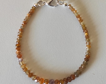 May include: A delicate bracelet composed of small, faceted, amber-colored gemstone beads in varying shades of orange, brown, and yellow. The strand is secured with a silver-toned metal lobster claw clasp and features small silver-toned spacer beads.