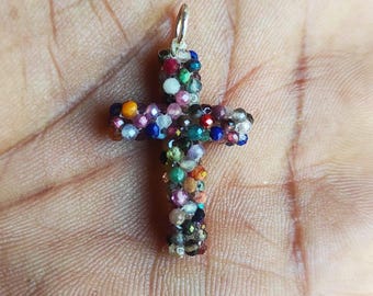 Puede incluir: Un colgante de cruz de plata hecho de pequeñas piedras preciosas de colores. La cruz está hecha de muchos colores diferentes, incluyendo rojo, azul, verde y amarillo.