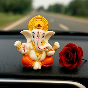 Könnte beinhalten: Eine kleine, weiß-orangefarbene Ganesh-Statue mit goldenen Akzenten und einer roten Rose. Die Statue hat einen Rüssel und große Ohren. Die Rose ist tiefrot und befindet sich neben der Statue.